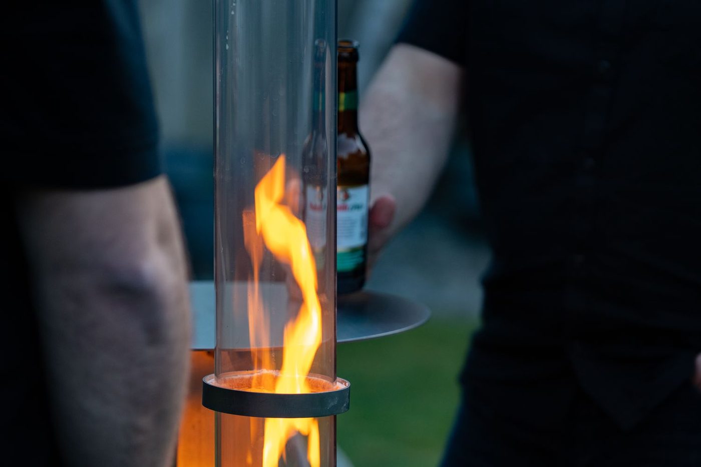 Flamme im Glasrohr der Rhönfackel, im Hintergrund Gäste mit Getränken